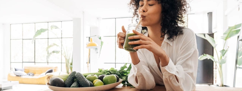 Young african american woman drinking green juice with reusable bamboo straw in loft apartment