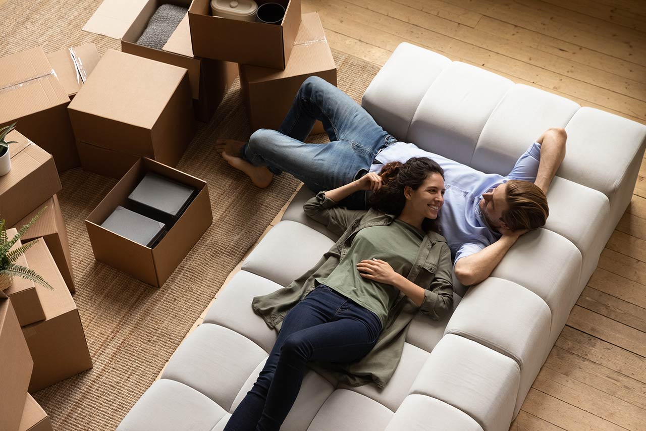 smiling couple resting on cozy couch with moving boxes