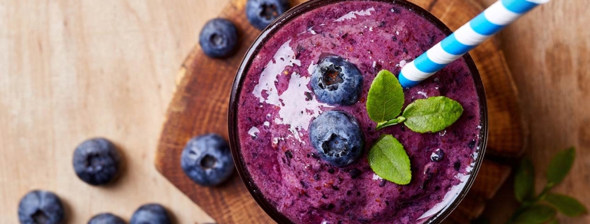 Glass of blueberry smoothie on wooden background from top view