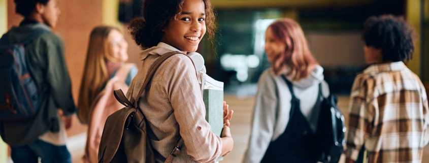 Happy African American high school student walking through hallway with her friends and looking at camera