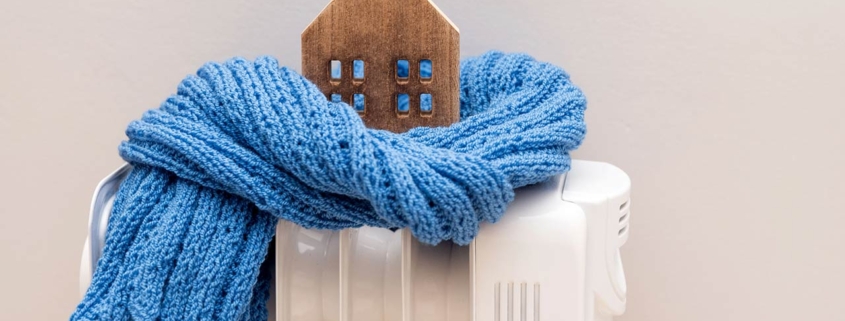 Wooden model house wrapped in a blue scarf on a radiator