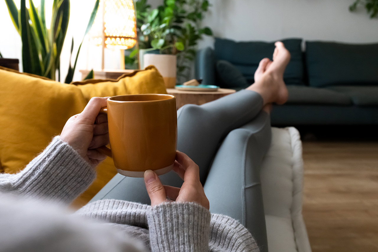 POV of young woman relaxing at home with cup of coffee lying on couch
