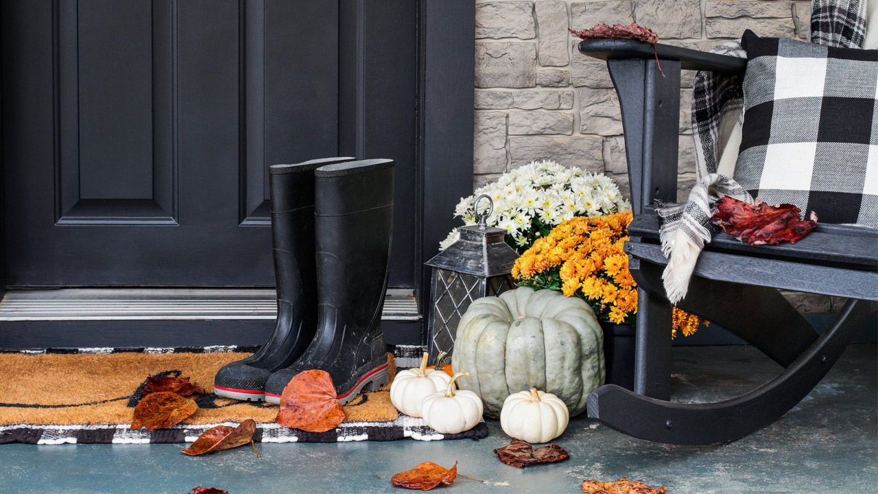 Traditional style front porch decorated for autumn with rain boots, heirloom gourds, white pumpkins, mums and rocking chair