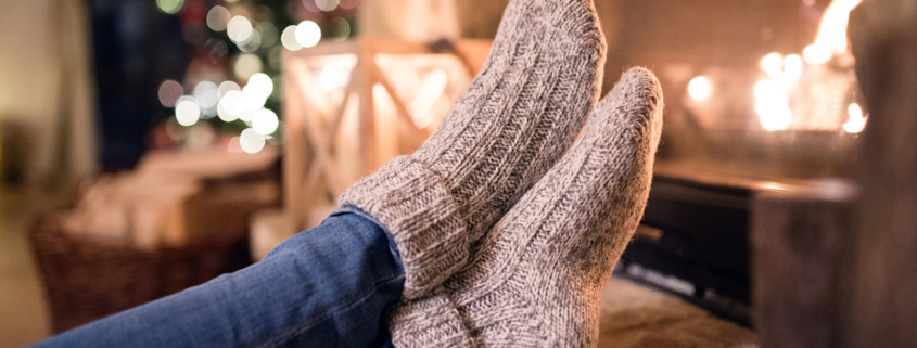 Feet of unrecognizable woman in woollen socks by the Christmas fireplace