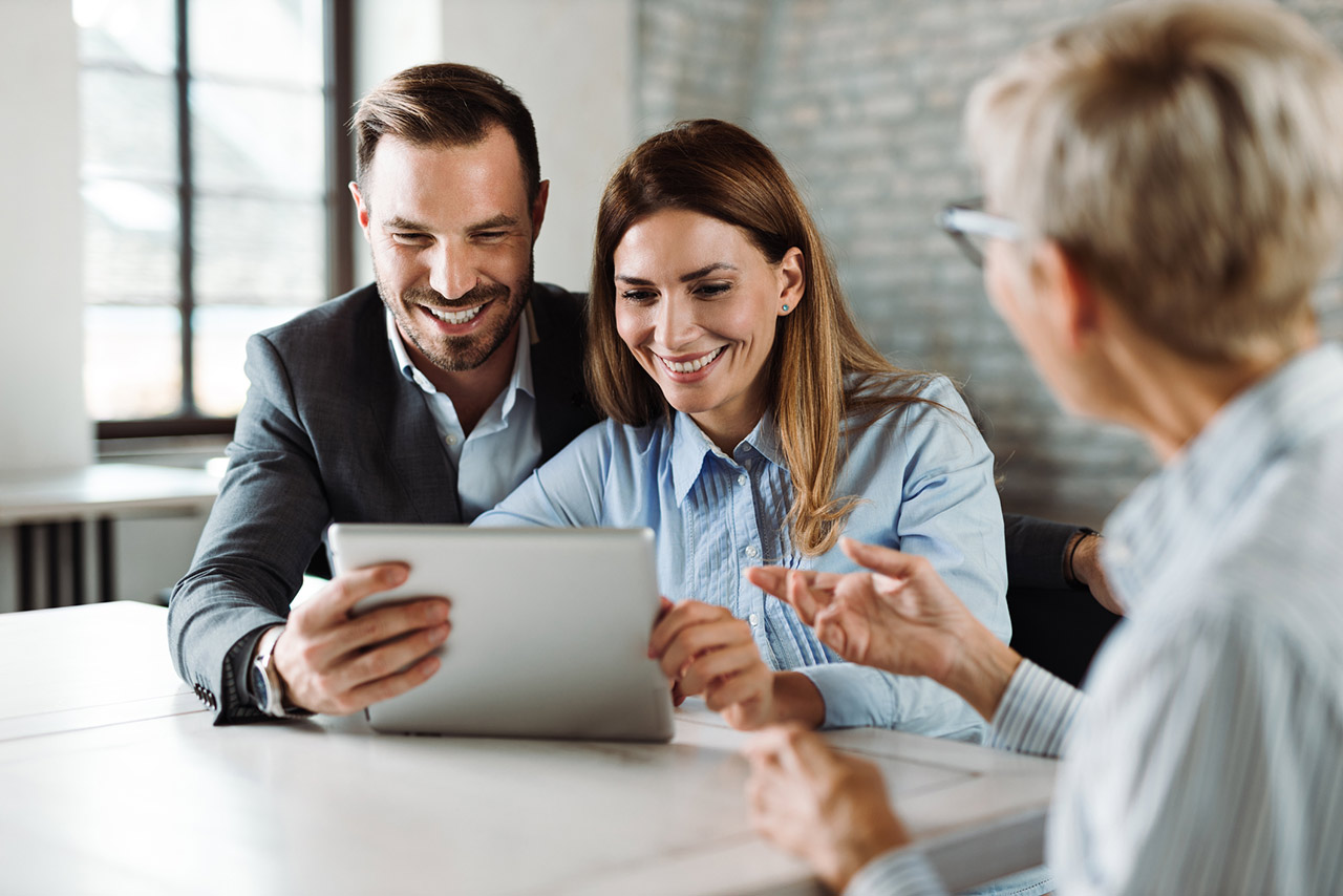 Happy couple using tablet while having a meeting with their real estate agent in the office